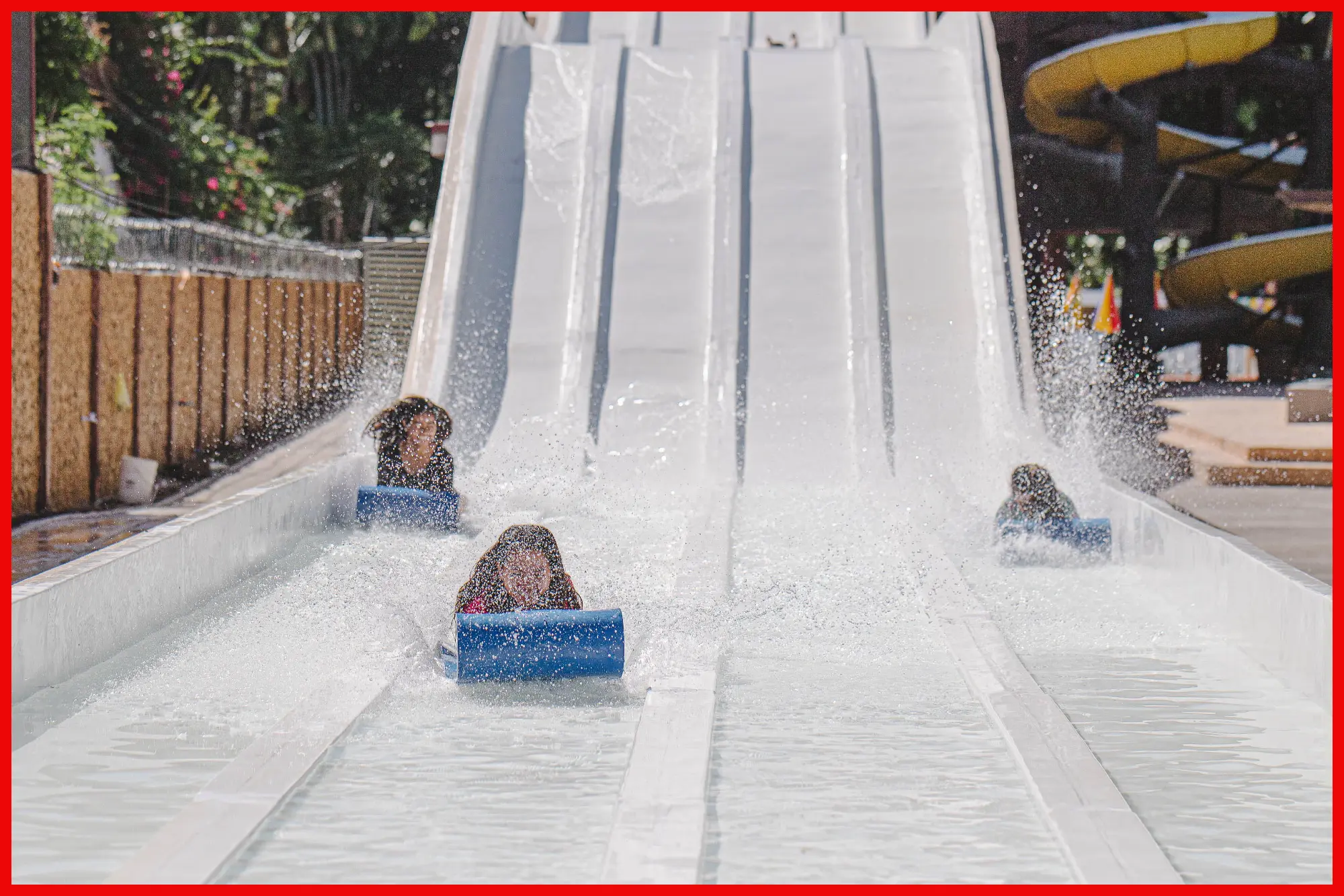 Excited riders descend a water slide making a big splash at the bottom, conveying the joy and excitement of a water park adventure